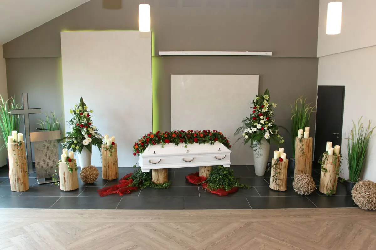 Aufgebahrter weißer Sarg mit roten Rosen in der Trauerhalle