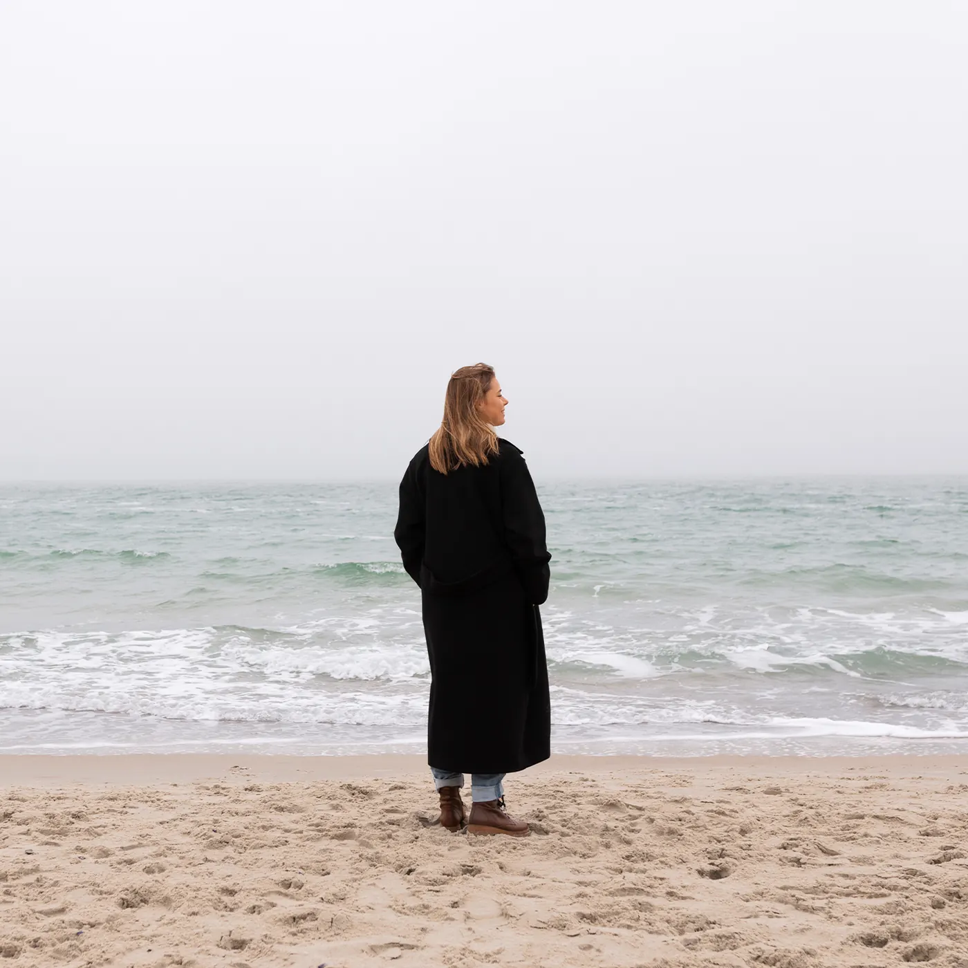 Frau im dunklen Mantel blickt aufs Meer